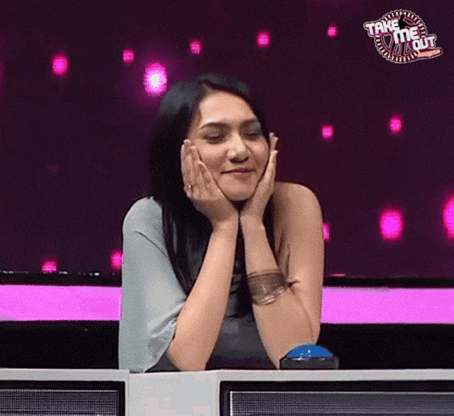 a woman is sitting at a table with her hands on her face and a take me out logo behind her