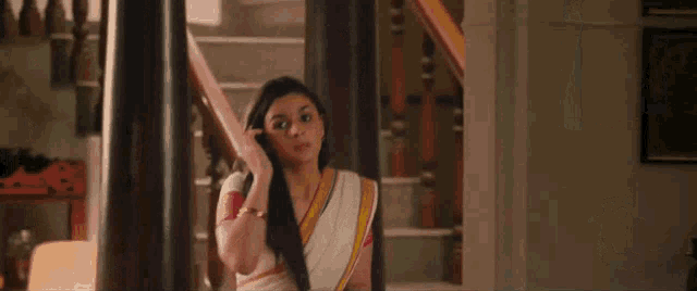 a woman in a white saree is standing on a set of stairs