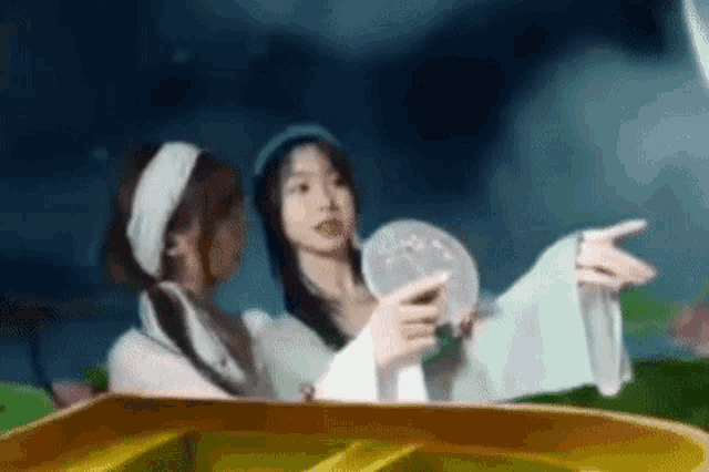 two women are standing next to each other in front of a piano . one of the women is holding a fan .