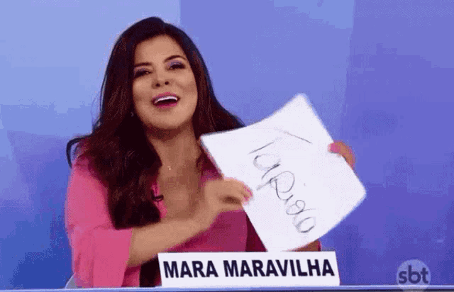 a woman in a pink shirt is holding a piece of paper that says ' mara maravilha ' on it .