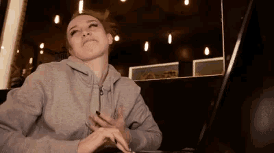 a woman in a grey hoodie is sitting at a table using a laptop computer .