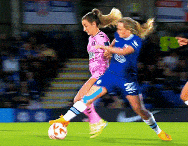 a female soccer player in a pink jersey with the letter k on it is being tackled by another player in a blue jersey