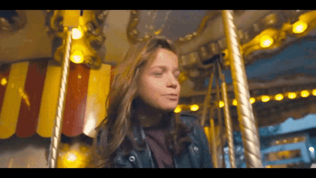 a girl is riding a merry go round with a yellow and red banner in the background