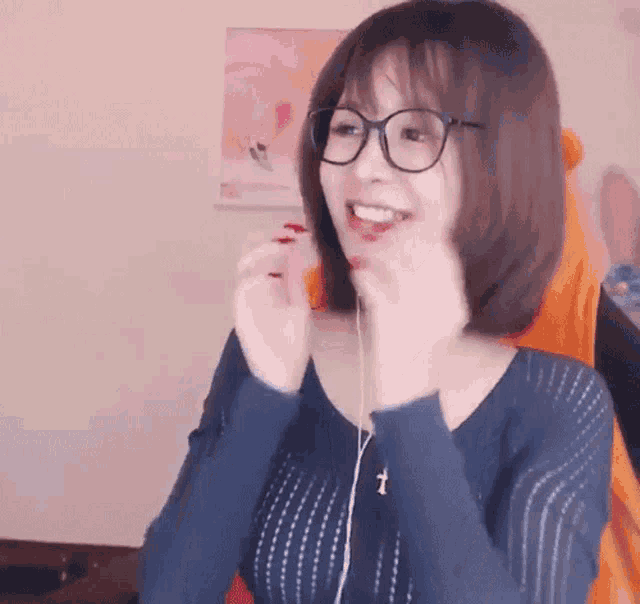 a woman wearing glasses and a blue sweater is smiling while sitting in a chair .