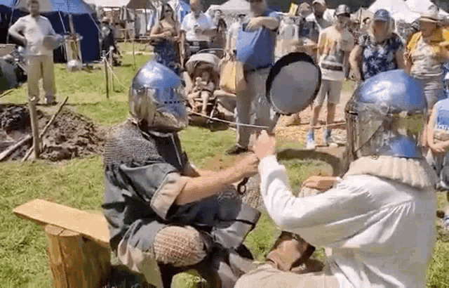 a man in a knight 's helmet is holding a pan over another man 's head .