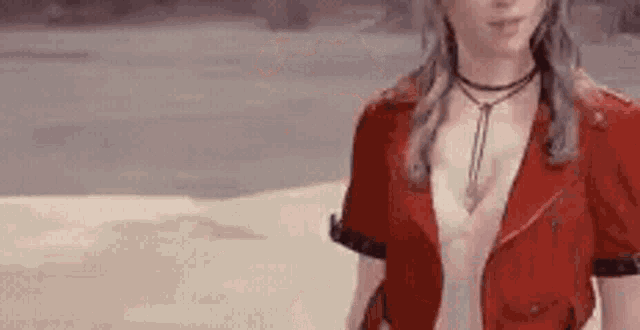 a woman wearing a red jacket and a choker is standing on a sandy beach .