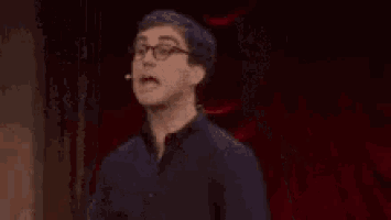 a man with glasses is standing in front of a red background