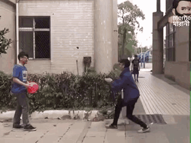 a man and a woman are playing frisbee on a sidewalk in front of a building .