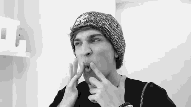 a man wearing a beanie has his fingers on his face