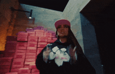 a woman wearing a pink hat and a black hoodie is standing in front of a pile of pink boxes
