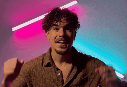 a man with curly hair and a beard is smiling in front of pink and blue lights
