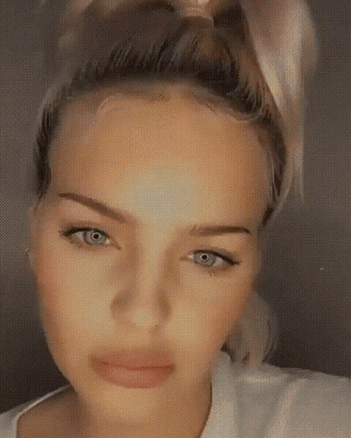 a close up of a woman 's face with a ponytail and blue eyes