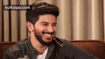 a man with a beard is smiling and laughing while sitting on a couch .