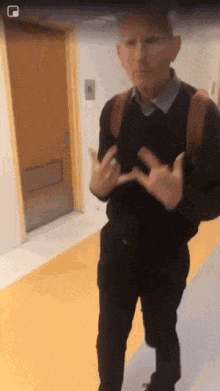 a man is standing in a hallway with his hands in his pockets and a backpack on his back .