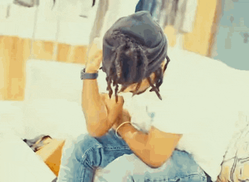 a man with dreadlocks is sitting on a bed with his head down .