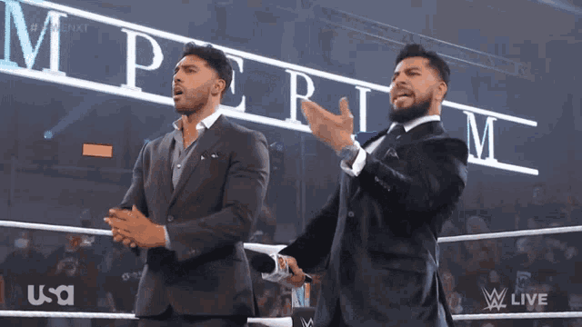two men in suits are standing in front of a sign that says perilm