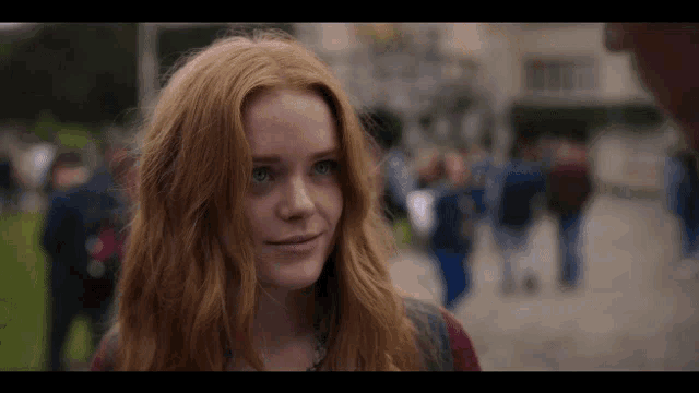 a girl with red hair and blue eyes is smiling in front of a crowd of people .