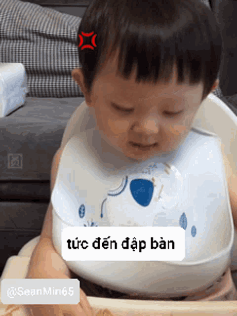 a baby wearing a bib with a koala on it is sitting on a high chair