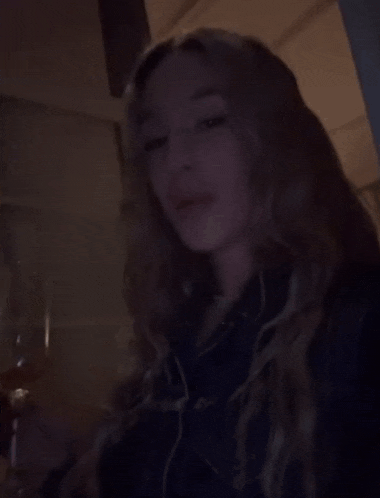 a woman is holding a glass of wine in the dark