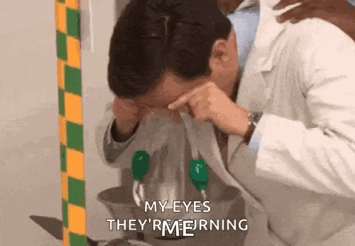 a man in a lab coat is washing his eyes with a hose .