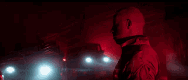 a man is standing in a dark room with red lights behind him and a bloody face .