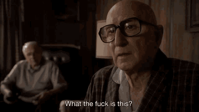 an elderly man wearing glasses is talking to another man in a chair .