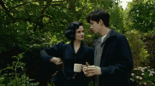 a man and a woman are standing next to each other in a garden with trees in the background
