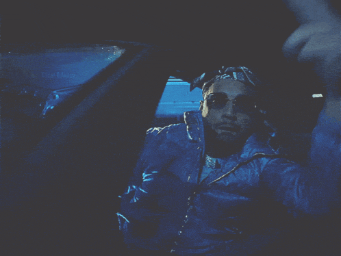 a man wearing sunglasses and a hat is sitting in a car with the word " the maw " on the window