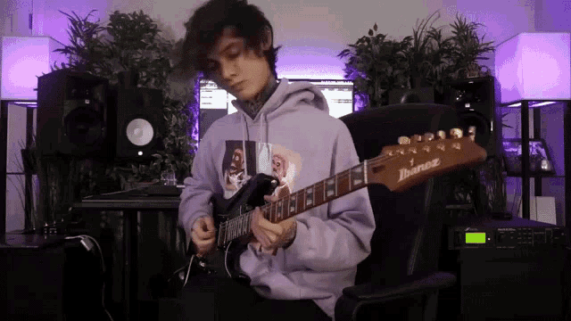 a man in a purple hoodie is playing an ibanez electric guitar