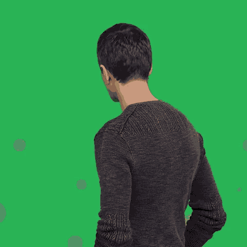 a man in a grey sweater is standing in front of a green screen
