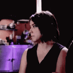 a woman in a black dress is sitting in a dark room looking at something .