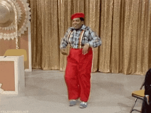 a man in red pants is dancing on a stage in front of a gold curtain .