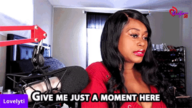 a woman sitting in front of a microphone with the words give me just a moment here above her