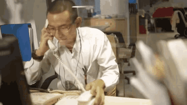 a man wearing glasses is talking on a telephone while sitting at a desk .