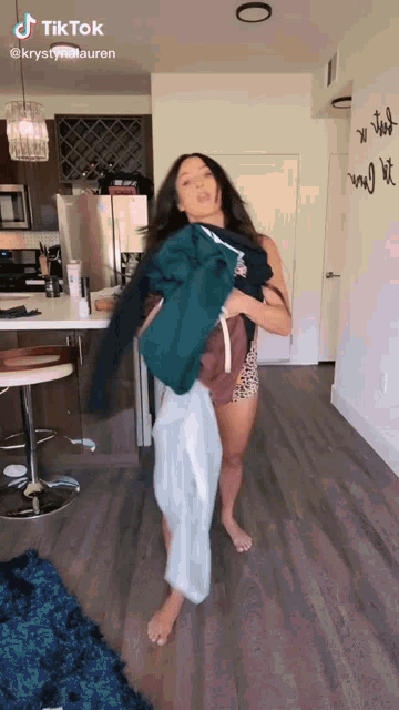 a woman is standing in a kitchen holding a sweater and a towel ..