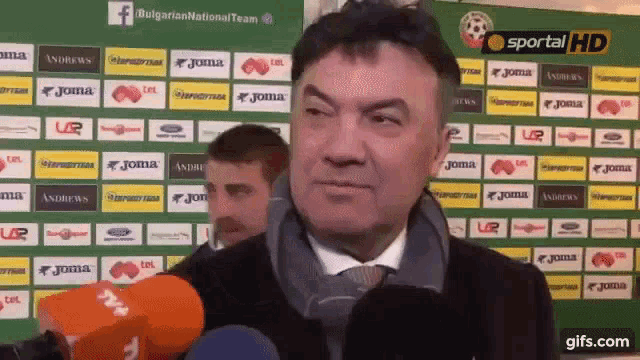 a man stands in front of a green wall with joma logos on it