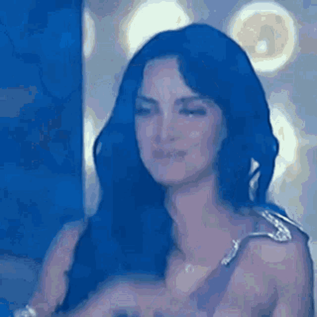 a woman with long blue hair is standing in front of a blue wall and smiling .