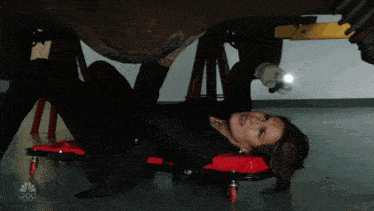 a woman is laying on a red rolling cart with the letters nbc on it