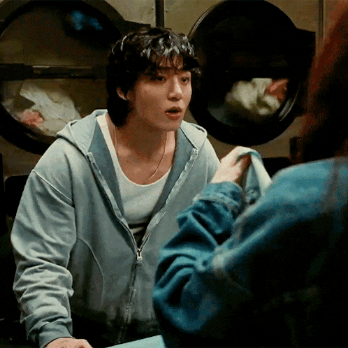 a man in a hoodie is talking to a woman in a laundromat