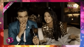 a man and a woman are sitting on a couch with a microphone in their hands .
