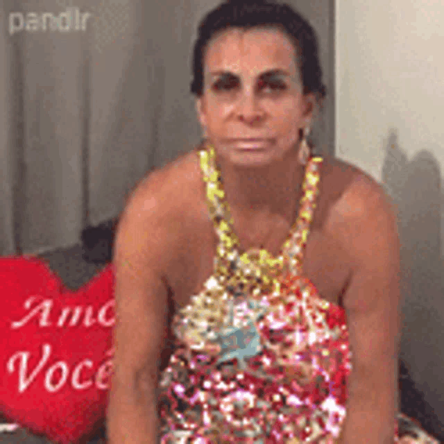 a woman in a dress is sitting on a couch next to a red pillow that says " amo você "