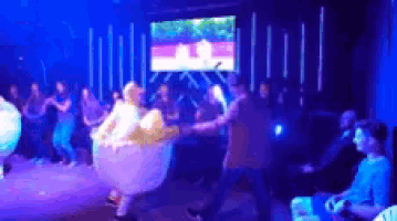 a group of people are dancing on a stage with a large screen in the background