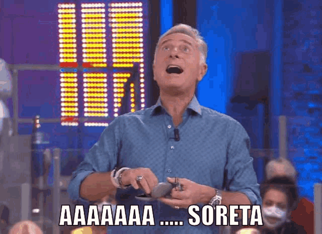 a man in a blue shirt is holding a cell phone and saying aa aaa soreta