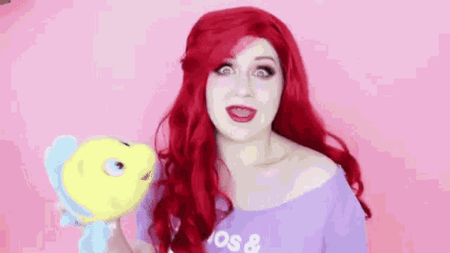 a woman with red hair is holding a stuffed fish and making a funny face .