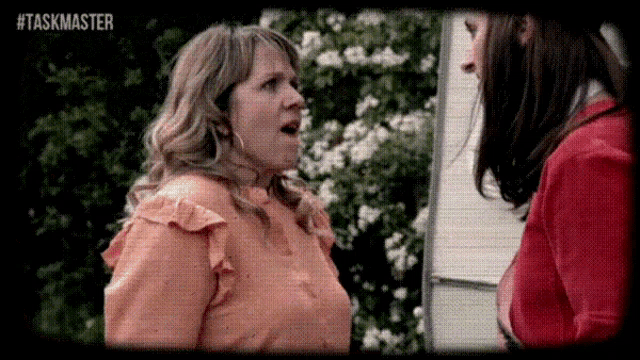 a woman in an orange shirt is talking to another woman in a red sweater outside .