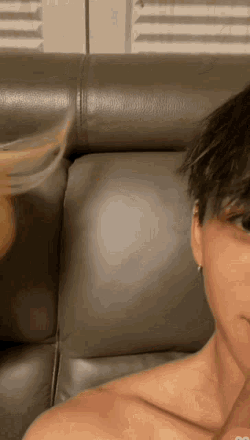 a man without a shirt is sitting on a couch looking at the camera
