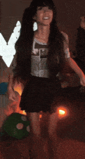 a woman in a black skirt is dancing in front of a green pillow