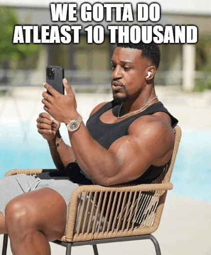 a muscular man is sitting in a chair looking at his phone with a caption that says we gotta do atleast 10 thousand