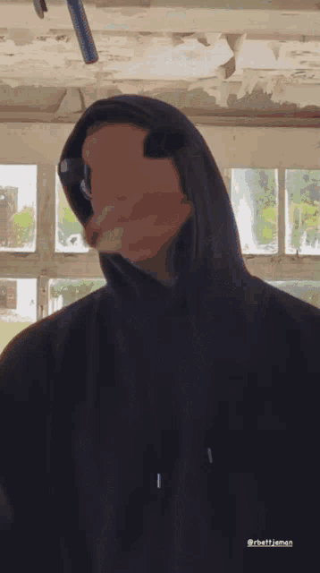 a man wearing a black hoodie and sunglasses is standing in front of a microphone