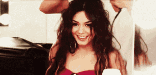 a woman in a red top is smiling while getting her hair done .